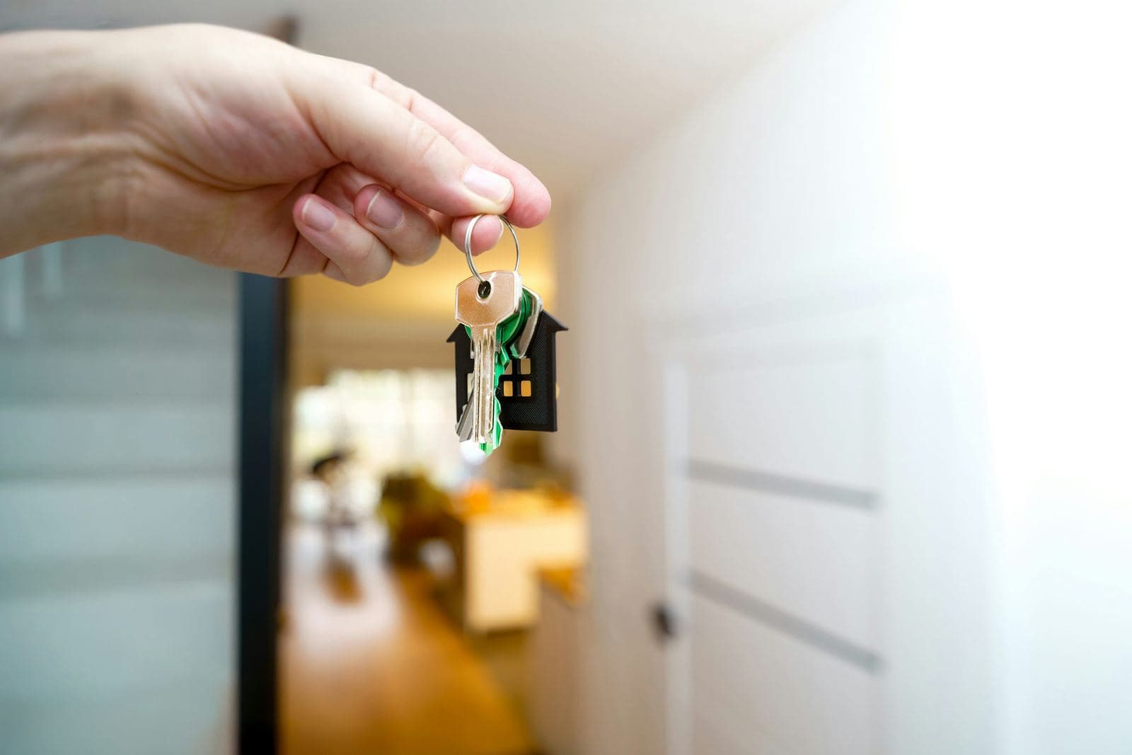 A hand holding a house-shaped keychain with keys in front of an open front door.