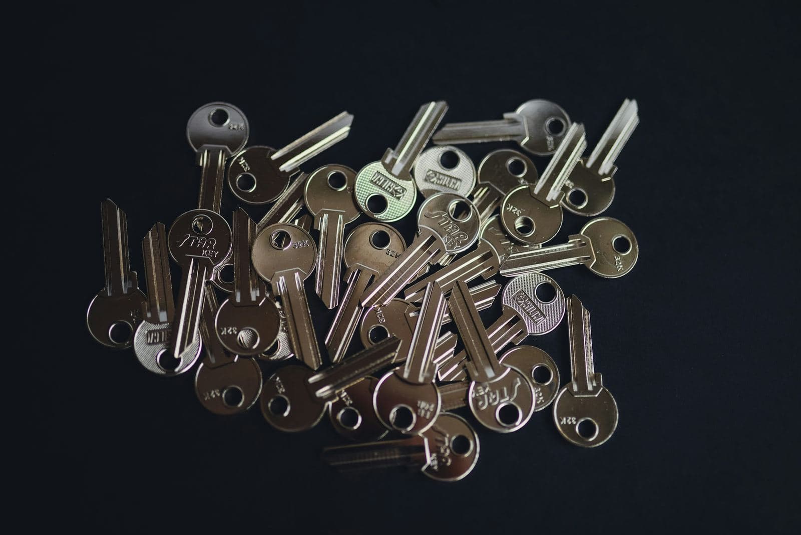 A large pile of duplicate blank house keys scattered on a dark surface.