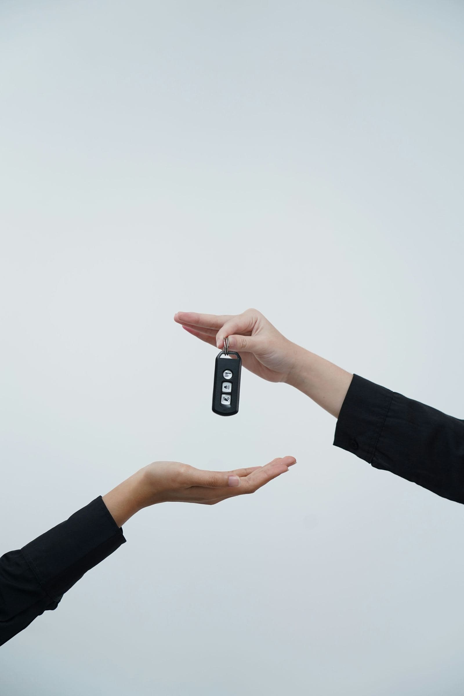 Two hands exchanging a black car key fob against a plain light gray background.