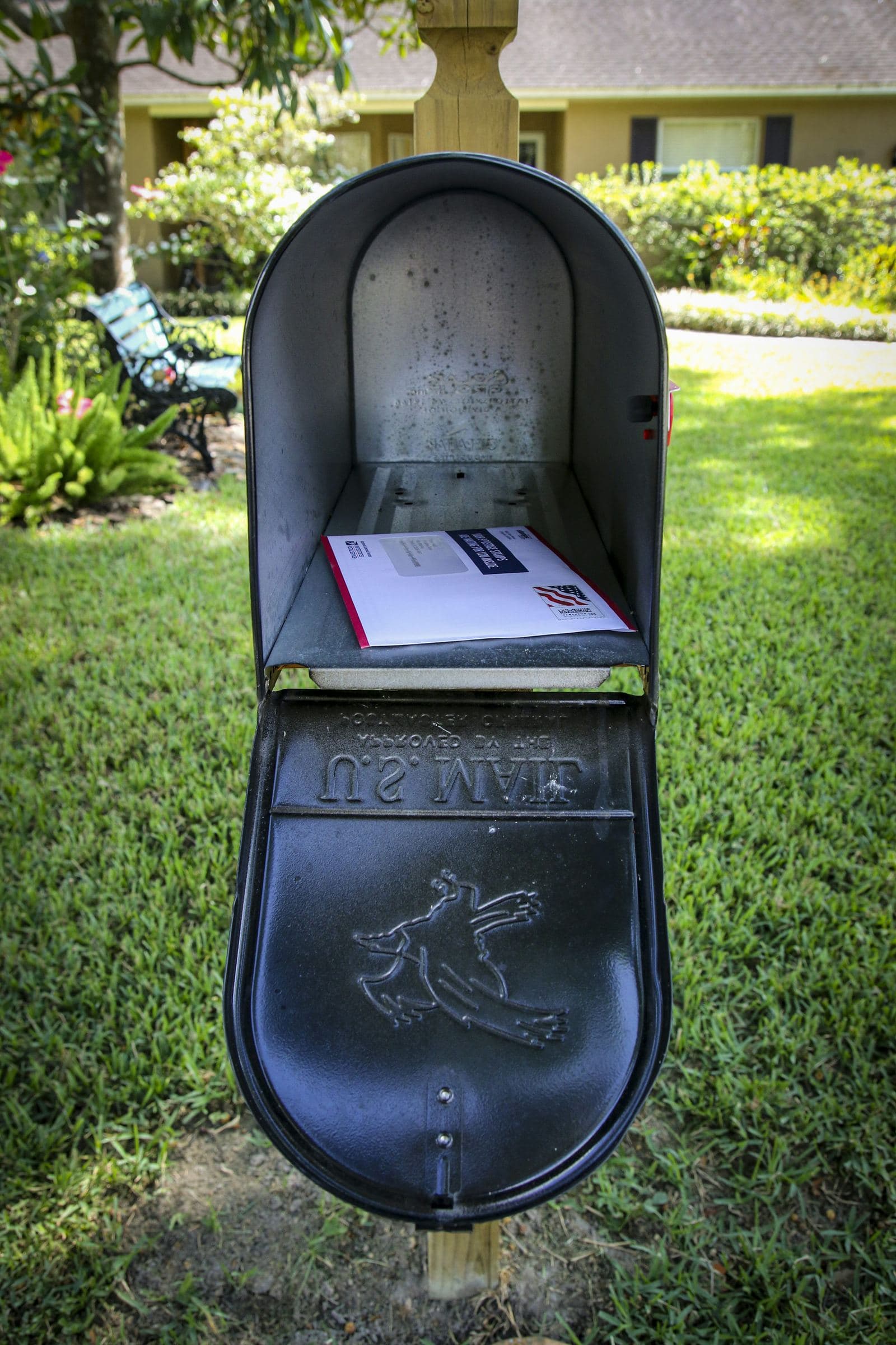An open residential curbside mailbox with mail inside, set against a green lawn.